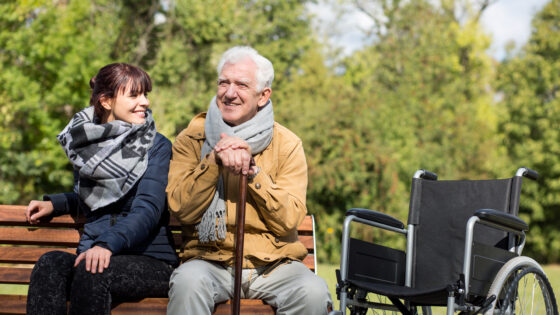 A daughter and her father sitting together on a bench, representing meaningful connection and self-care for family caregivers.