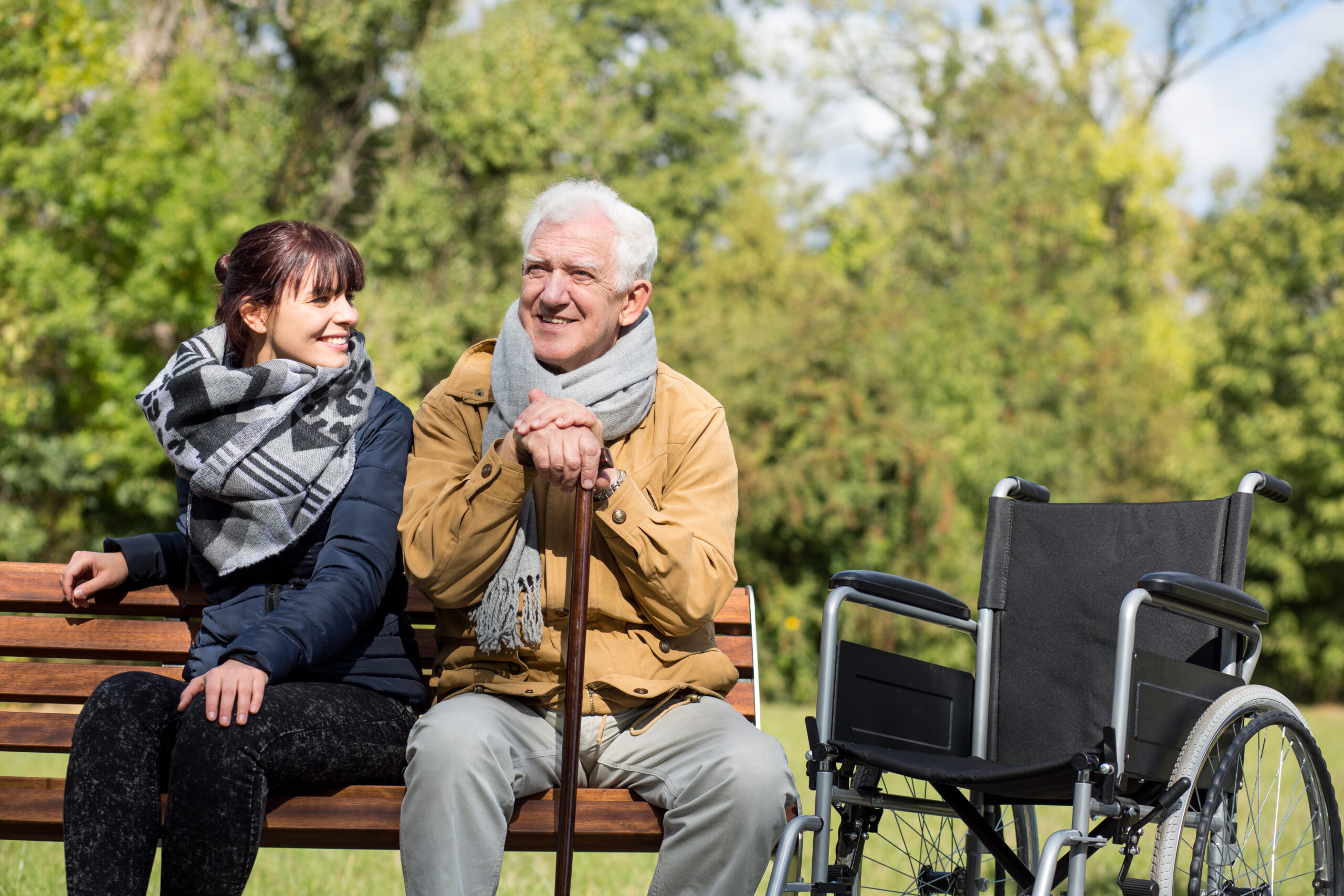 A daughter and her father sitting together on a bench, representing meaningful connection and self-care for family caregivers.