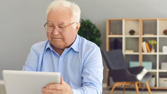 Older man using a tablet at home to stay connected and manage support while aging independently.