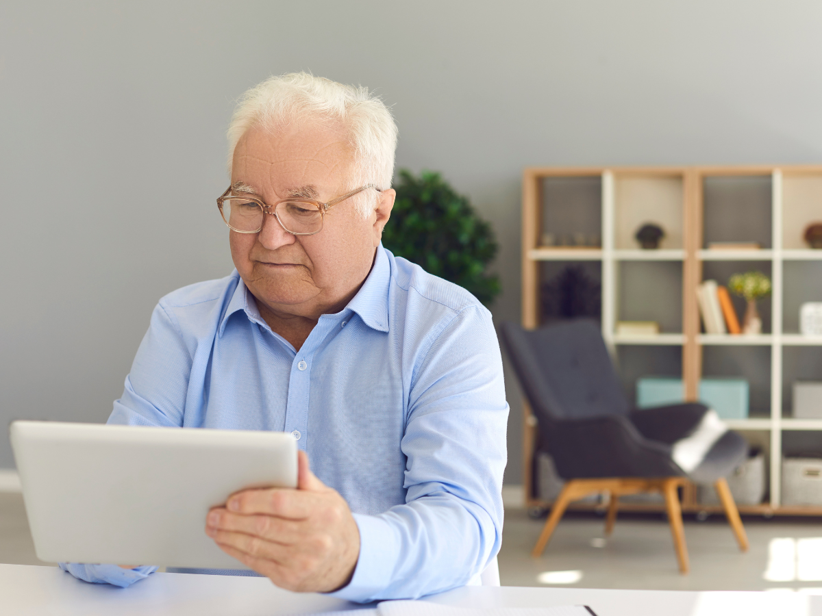 Older man using a tablet at home to stay connected and manage support while aging independently.