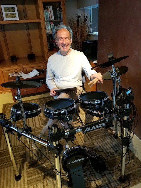 Dr. Joe Casciani smiling while playing a drum set as part of an active and engaged lifestyle.
